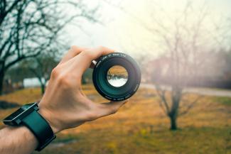 Person holding a camera lens in a field. The view of the field within the camera lens is upside down.